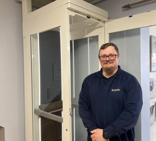 Terry Lifts CAD Technician stood in front of an affinity home lift model in the factory showroom.